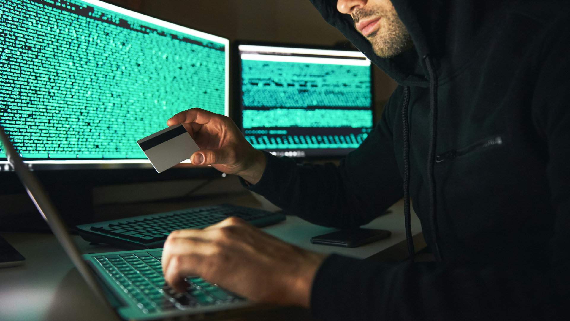 Betrüger mit Kapuze nutzt gestohlene Kartendaten an einem Laptop