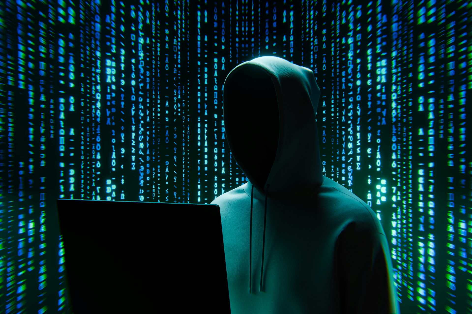 Vermummte Silhouette vor grün-blauen Datenströmen